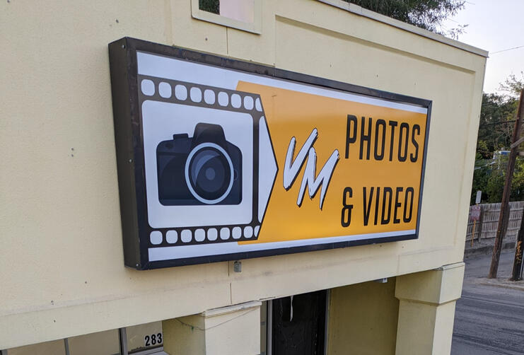 Wall-mounted acrylic sign reading ‘VM Photos & Video’ with camera graphic and yellow background, newly designed and refaced.